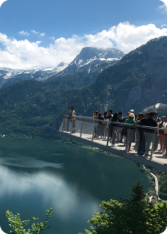 Besucher auf Aussichtsplattform über dem Hallstätter See mit Blick auf verschneite Alpen.