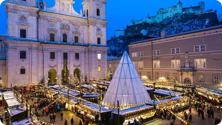 Abendaufnahme des Salzburger Christkindlmarkts mit Lichtern, Dom und Festung Hohensalzburg im Hintergrund.