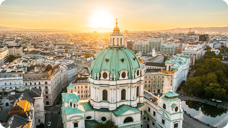 Luftaufnahme der Wiener Karlskirche bei Sonnenuntergang mit Blick über die Stadt.